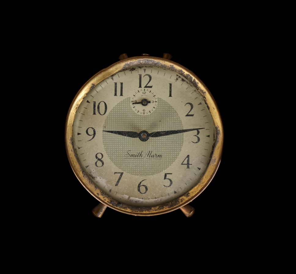 Small round alarm clock with the time stopped at 9:13 against a black background