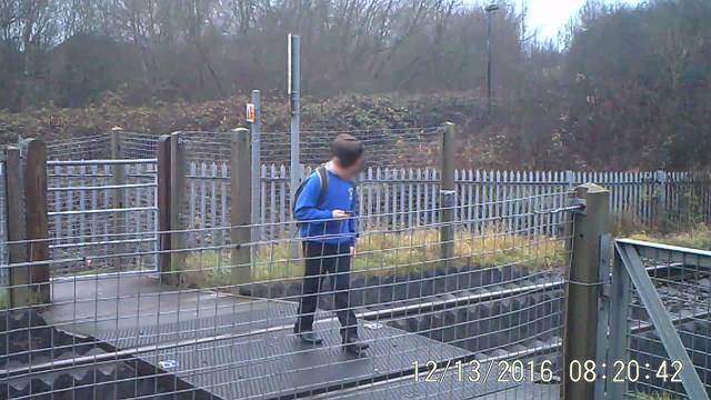 A schoolboy looks at his mobile phone while crossing the railway line at Griffin Lane, Aylesbury