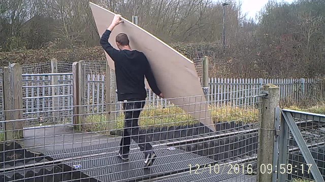 A man carries a large piece of building material over the level crossing at Griffin Lane, Aylesbury