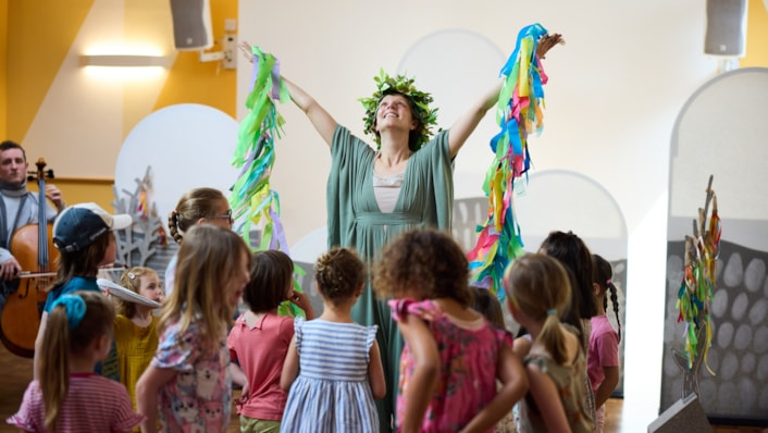 FestivalofPlay - Speedwell Dance: Image shows a woman with holding ribbons with her arms pointed to the sky, surrounded by children.