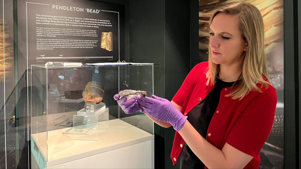 Sarah Austin, curator at Lancashire Museums, holds a silver armlet from the 'Silverdale hoard,' one of the largest Viking hoards ever discovered in the UK, which consists of jewellery, silver ingots and coins. In the background is the display of the 'Pendleton bead,' a rolled gold bead dating to c.2