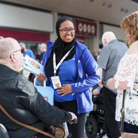 Big Event staff member: Big Event staff member where's blue Motability Scheme fleece and smiles at two customers