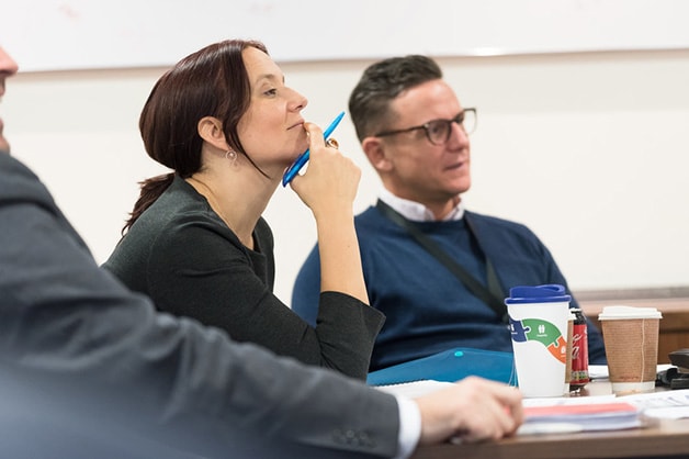 gpg-report-image: Side view of woman in business meeting. She holds a pen in her hand and rests chin on the same hand