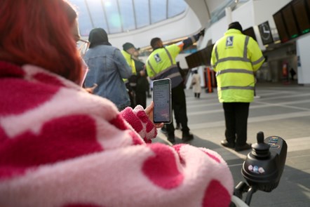 A woman with pink hair holding her phone, which is displaying a WhatsApp message, at Birmingham New Street station.