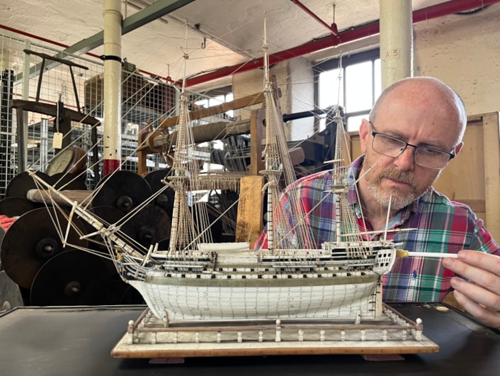 Model ships: Curator John McGoldrick with an intricate model ship carved from bone by a French prisoner during the Napoleonic Wars.
Complete with an elaborate figurehead, planked deck and carved helm with a steering gear and compass box, the bone model dates from the early 19th century and is believed to be an example of the type carved by French captives held in British prisons and aboard ships.