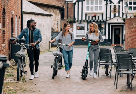 On the left of the picture is a young male pushing a Beryl bike, in the centre is a young female also pushing a Beryl bike and on the right is a young female pushing a Beryl e-scooter.