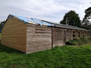 sancton Village Hall 1: Sancton Village Hall under construction with wooden exterior, blue tarp on the roof, set amid greenery and trees.