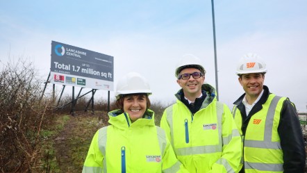 The three people in the photo caption are stood together wearing hard hats and high viz jackets, with the sign in the background.