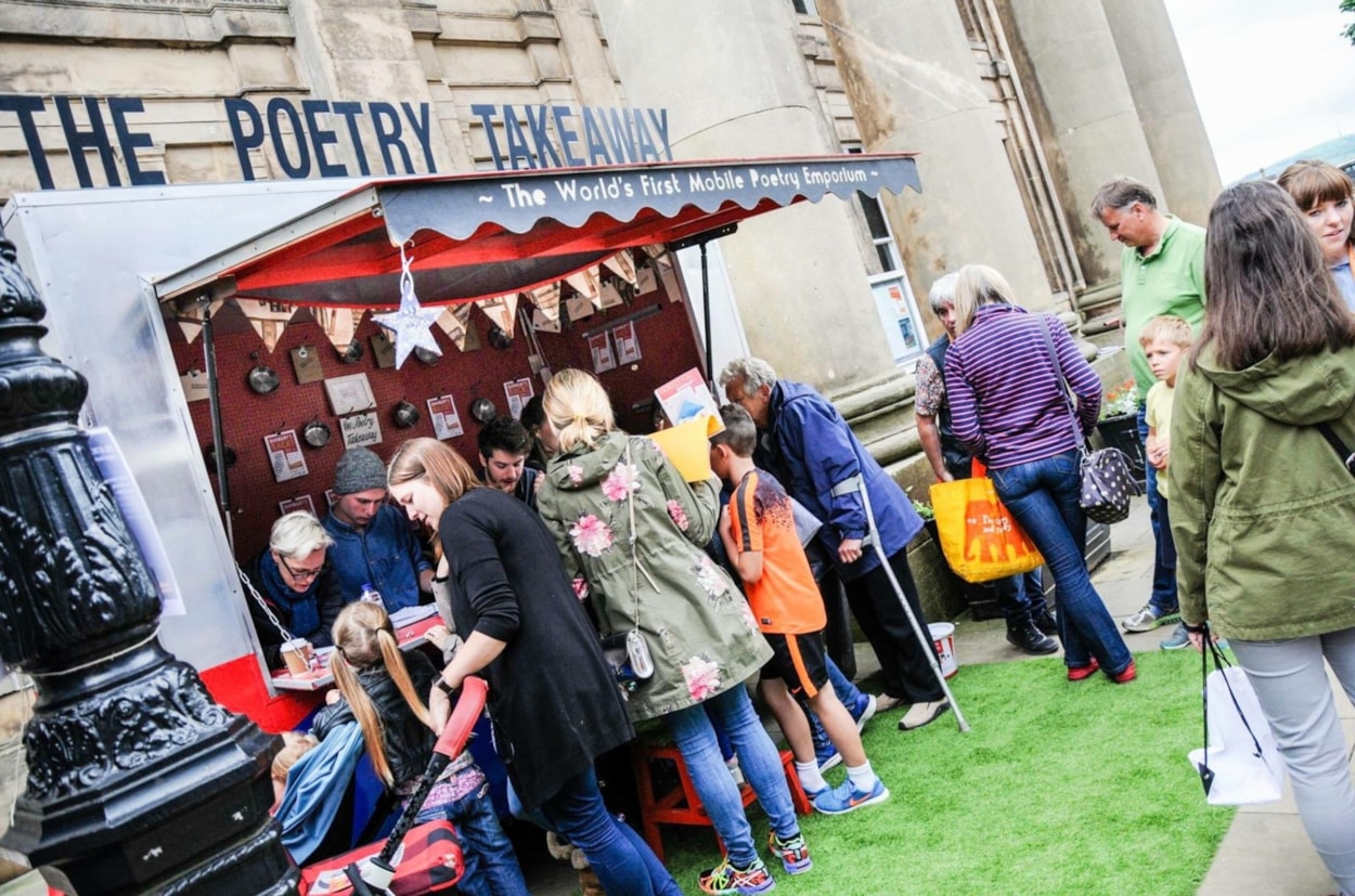 Poetry Takeaway: A group of people of different ages gather around the Poetry Takeaway mobile vehicle.