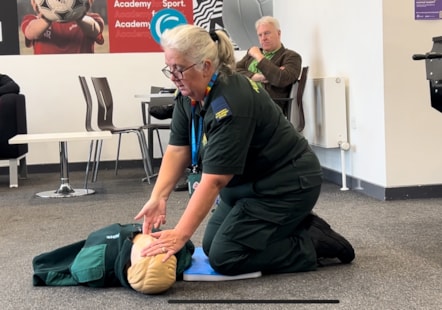 Alex Mason knelt down with dummy, lifting it's chin with 2 fingers to open its airways for resuscitation.