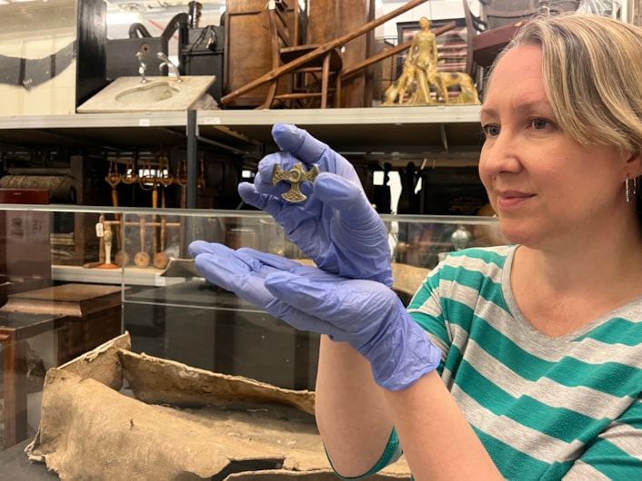 Saxon cross: Kat Baxter, Leeds Museums and Galleries' curator of archaeology with the Saxon pendant.
Believed to date from the eighth century, the gilded pectoral cross may have once been a badge of office for an important church leader or official and was unearthed last year by a metal detectorist.
With one arm broken, and the central stone now missing, the cross is nevertheless a stunning example of metalwork, made from solid silver covered with a thin layer of gold leaf.
In the background is a lead coffin which was buried for more than 1,600 years before it was discovered in a previously unknown cemetery site near Garforth alongside the remains of more than 60 individuals from late Roman to early Saxon periods.