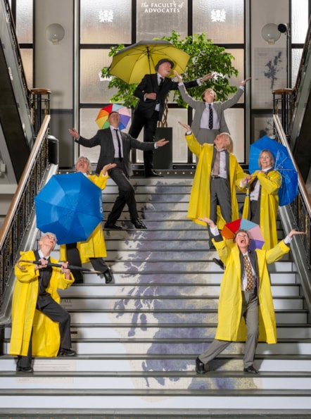 A group of dancers dressed in suits and raincoats post with colourful umbrellas on a set of stairs which has a map of Scotland printed on it