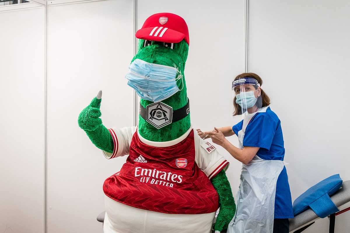 Arsenal mascot Gunnersaurus (left) gets a Covid-19 jab from a frontline member of staff at an Islington vaccination centre