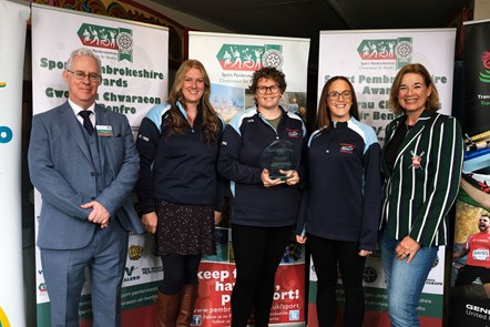 Women from the Wiseman's Bridge Coxed Squad happily holding their award, with Stephen Thornton.