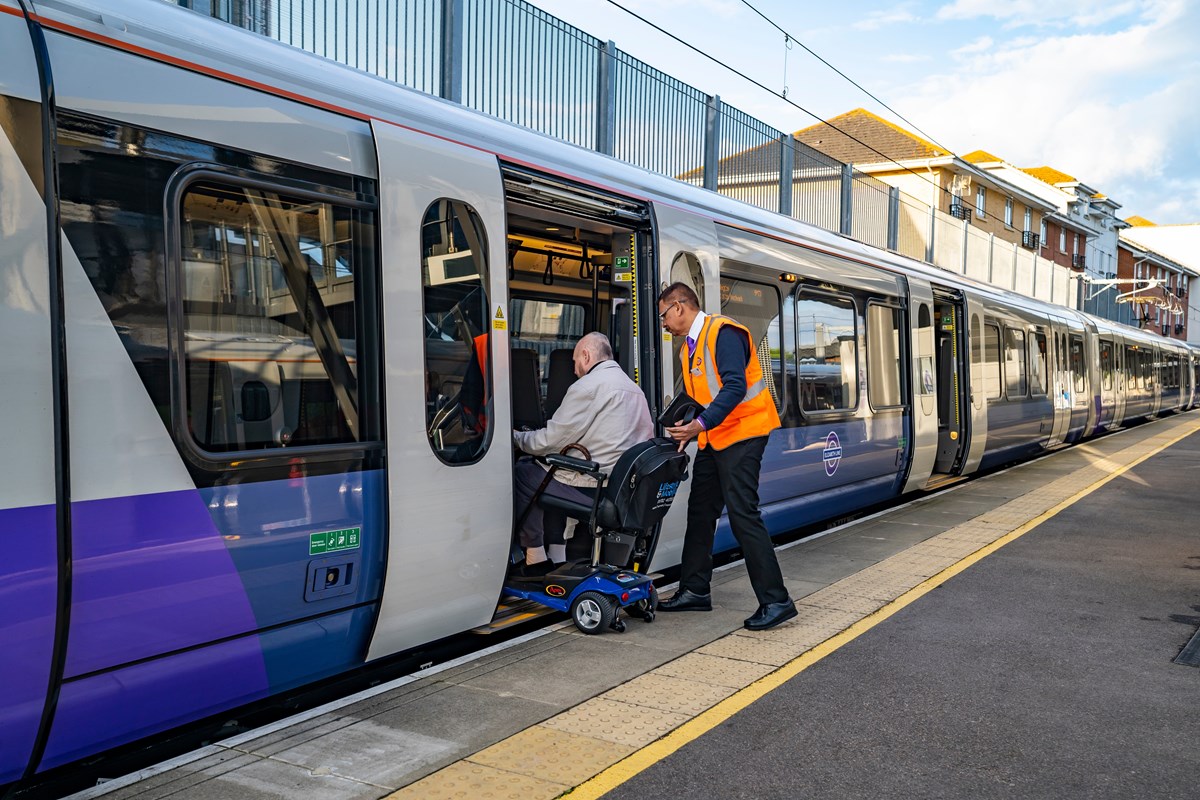 Man in wheelchair being assisted by platform staff to board a train