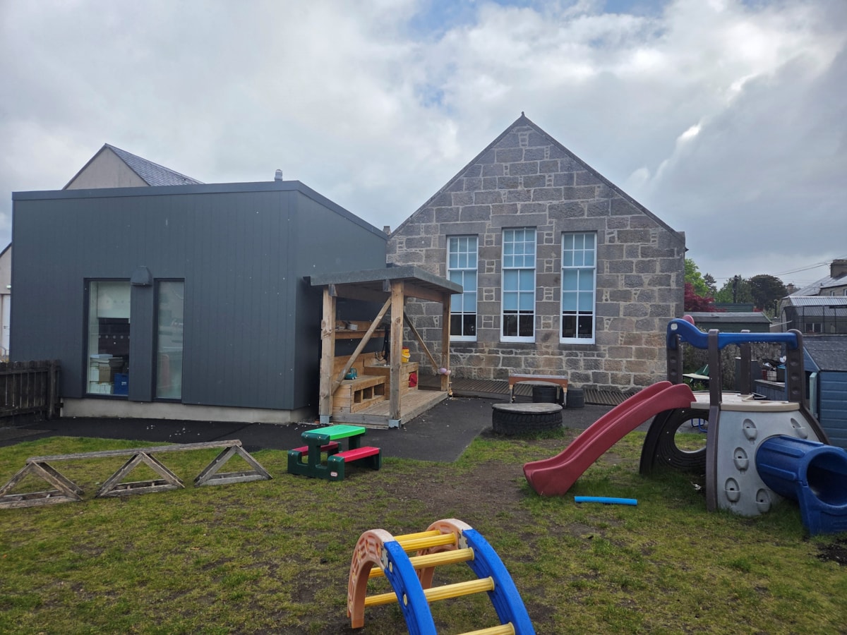 Photo of the outdoor play area at Aberlour Primary Nursery with climbing equipment, slide and the nursery building in the background.