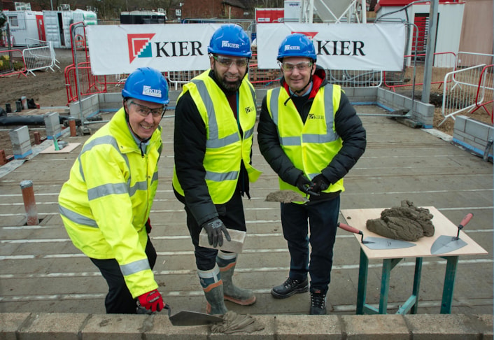 Yeadon care home: Image shows three men, in high vis jackets, by a low brick wall, with two holding a trowel and one holding a brick.