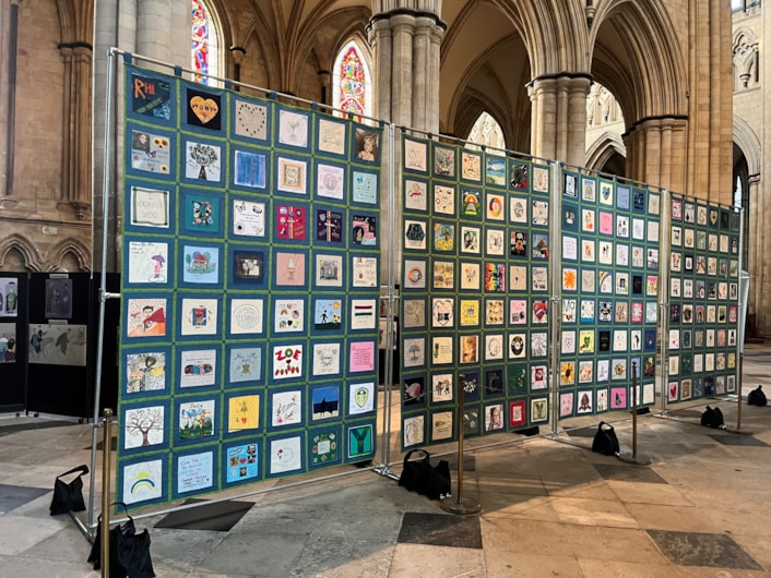 Baton of Hope Leeds tour 3: Four panels of the quilt are shown hanging in a church, featuring 10cm by 10cm memorial squares in honour of lost loved ones.