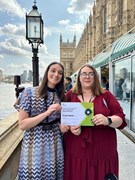 Mia Sandells and Georgia Hescott receive their award: Two women in front of the Houses of Parliament holding an award