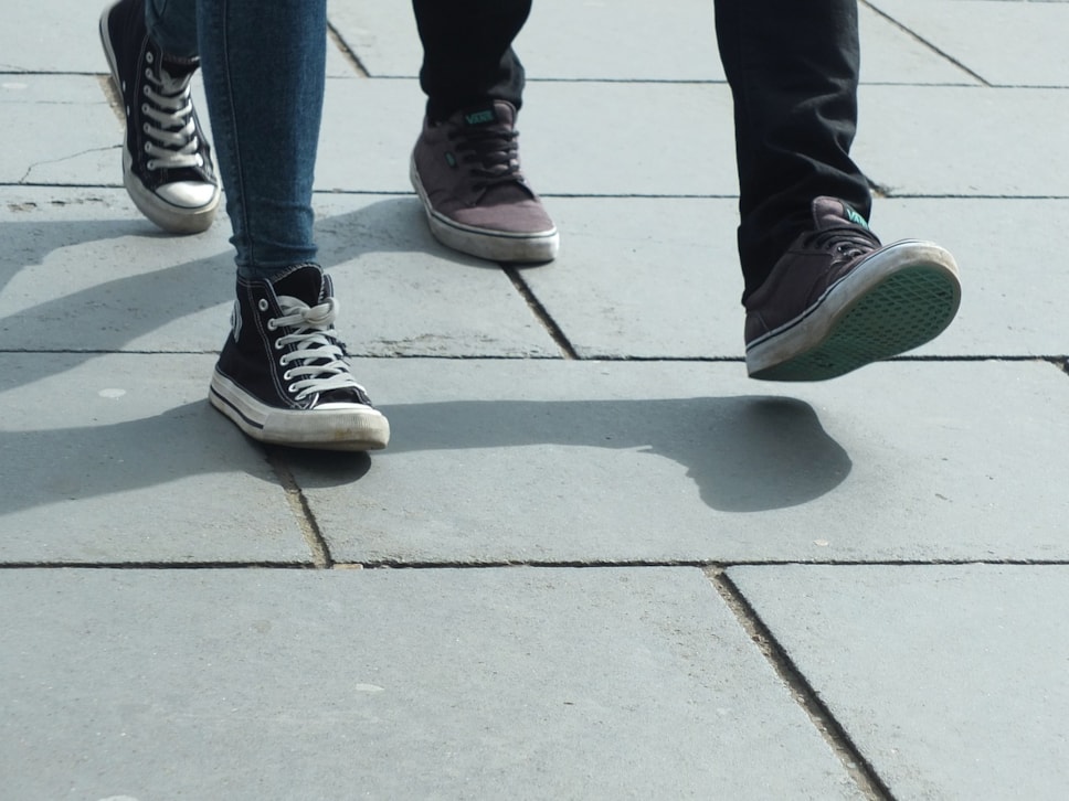 two sets of feet in trainers walking on paving slab path