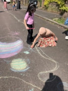 PlayStreet ChalkDrawing2: Two young girls drawing on the road with colourful chalk.