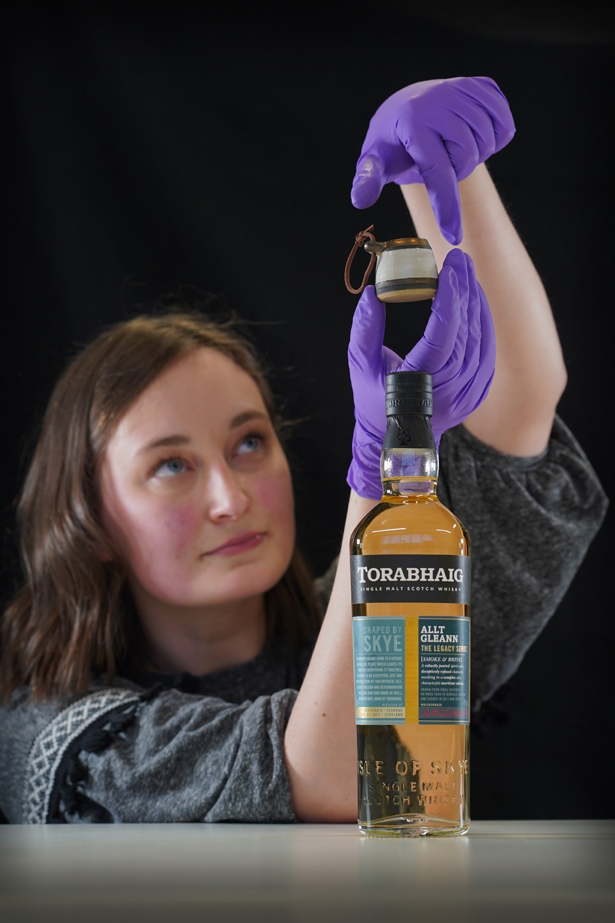 Doctoral Researcher Laura Scobie, with a ceramic measure created by Katharina Lenz and bottle from Torabhaig Distillery. Photo © Stewart Attwood.