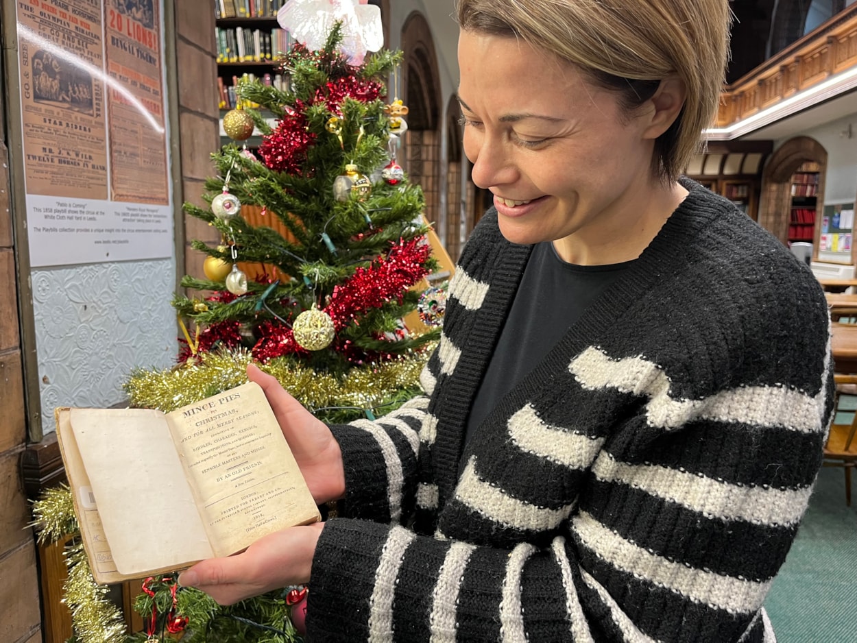 Library Christmas display: Library and digital assistant Anna Jones with a book of children’s Christmas games from 1812 entitled Mince Pies for Christmas. Filled with riddles and games, the book claims ‘to exercise the ingenuity of all sensible masters and misses.’
Some of the charades within its pages have been circled by the children who must have  played the game with their families at Christmas more than 200 years ago.