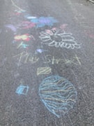 PlayStreet ChalkDrawing1: Chalk drawings of flowers on the road. The word 'Play Street' is also written in chalk.