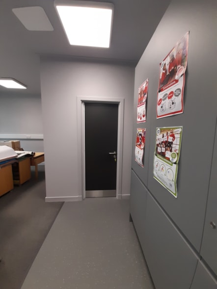 Refurbished school interior with grey flooring, a dark door, bright ceiling lights and educational posters.