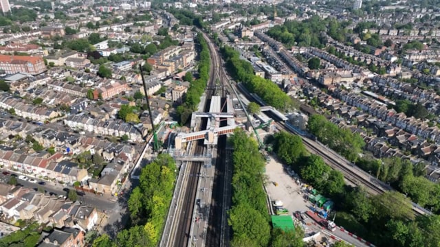Wider aerial view of Hither Green accessible footbridge being lifted into place: Wider aerial view of Hither Green accessible footbridge being lifted into place
