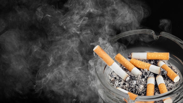 Stop Smoking: Image shows a close up of an ashtray with a still-smoking cigarette propped in, among ends of old cigarettes.