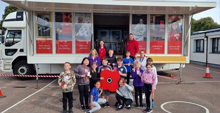 A happy group from Poppyscotland and Seafield Primary School in Elgin gather at Bud the Poppy bus with a large poppy.
