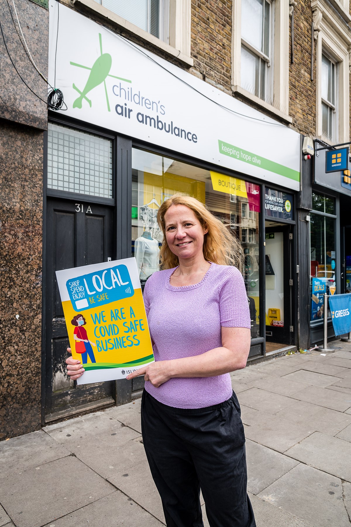 Joanna Phillips, manager of the Children's Air Ambulance charity shop in Junction Road, Archway, promoting the Covid-Safe Business Award scheme window stickers