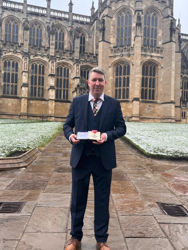 Michael Brodie holding his CBE and standing outside Windsor Castle