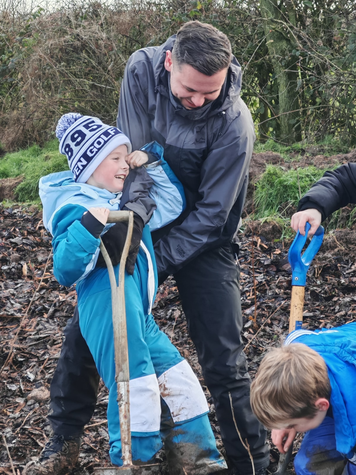 Councillor Joshua Roberts helps a youngster stuck in the mud while planting trees