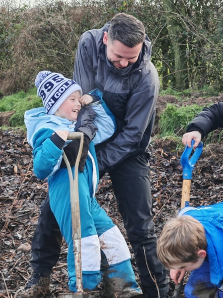 Councillor Joshua Roberts helps a youngster stuck in the mud while planting trees