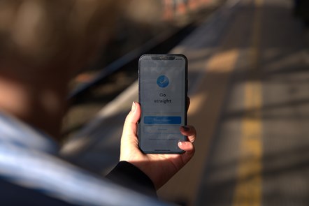 A woman holds a phone in her left hand in front of her, which displays directions, on the station platform.