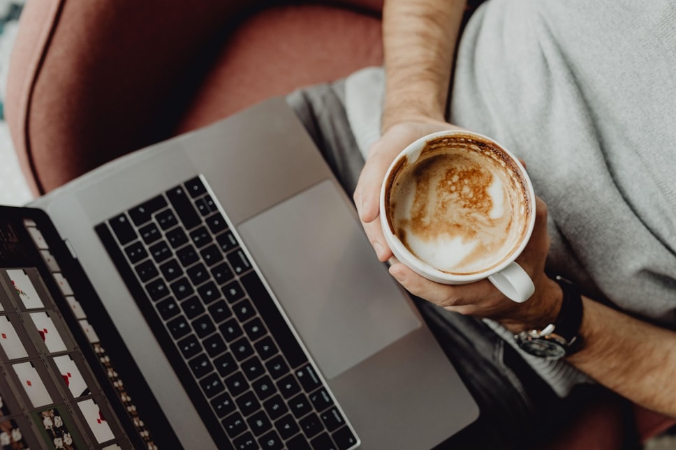 man holding cup of coffee with laptop, shot from above