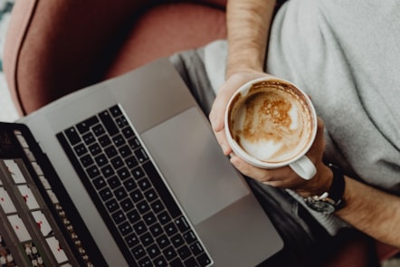 man holding cup of coffee with laptop, shot from above