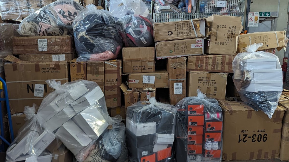 Items seized from the address in Skelmersdale, including black/orange and white shoe boxes in clear bags; pink, black and beige counterfeit Adidas clothing and large cardboard boxes bound with packing tape