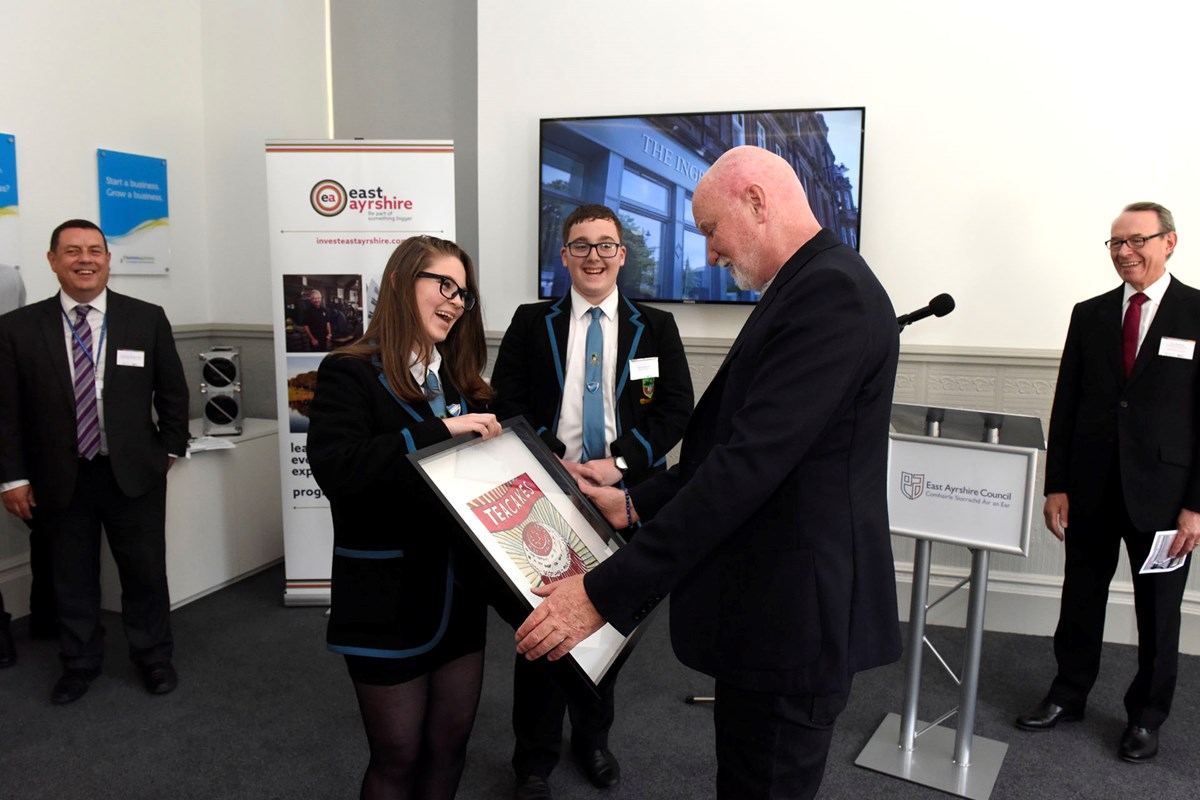 Eilidh McHattie and Ryan Bartolo (Sir Tom Hunter enterprise challenge winners from Doon Academy) present Sir Tom with a gift painted by Erin Barr from Doon Academy