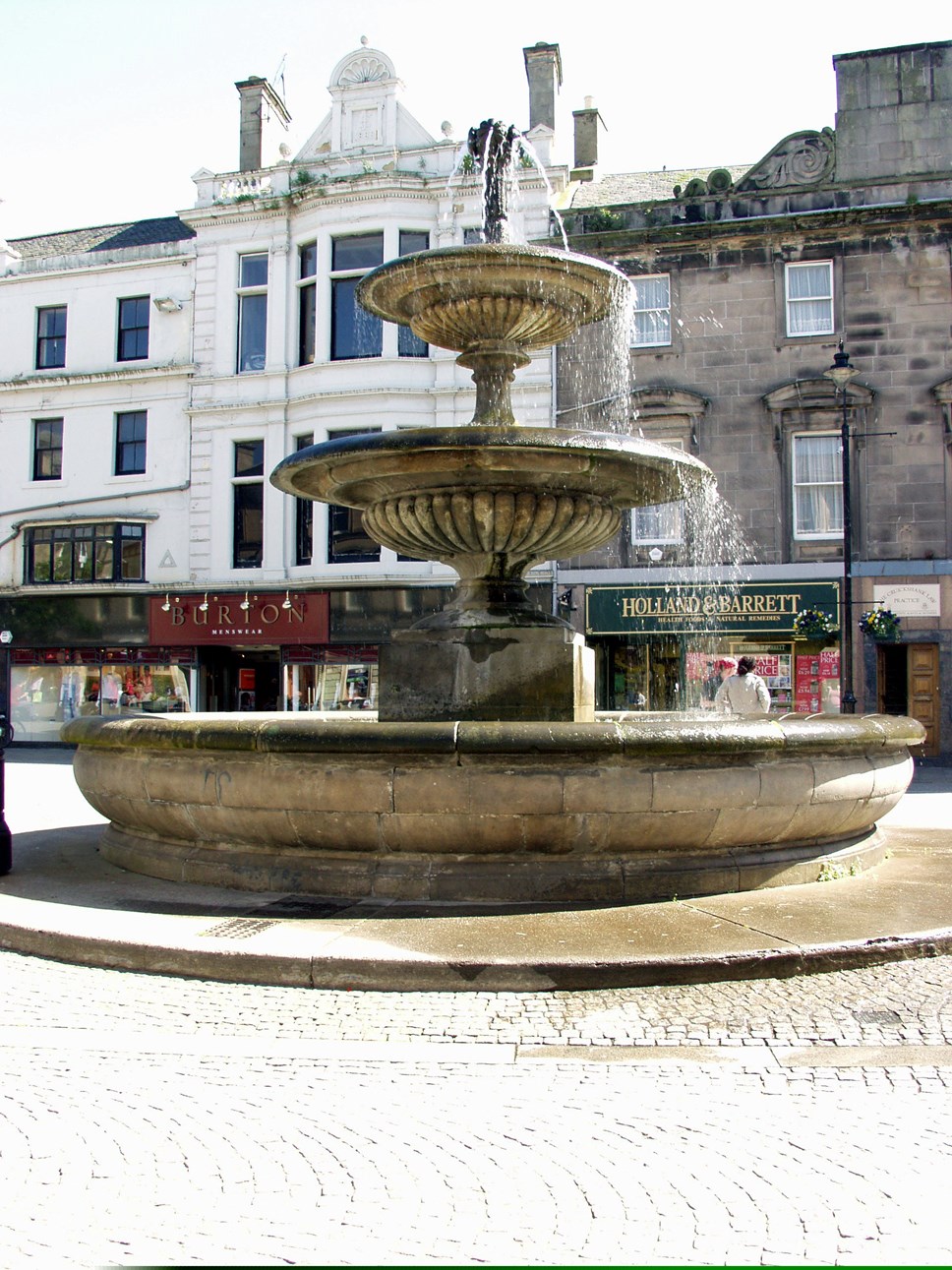 Water cascades down a three-tiered beige stone town centre fountain