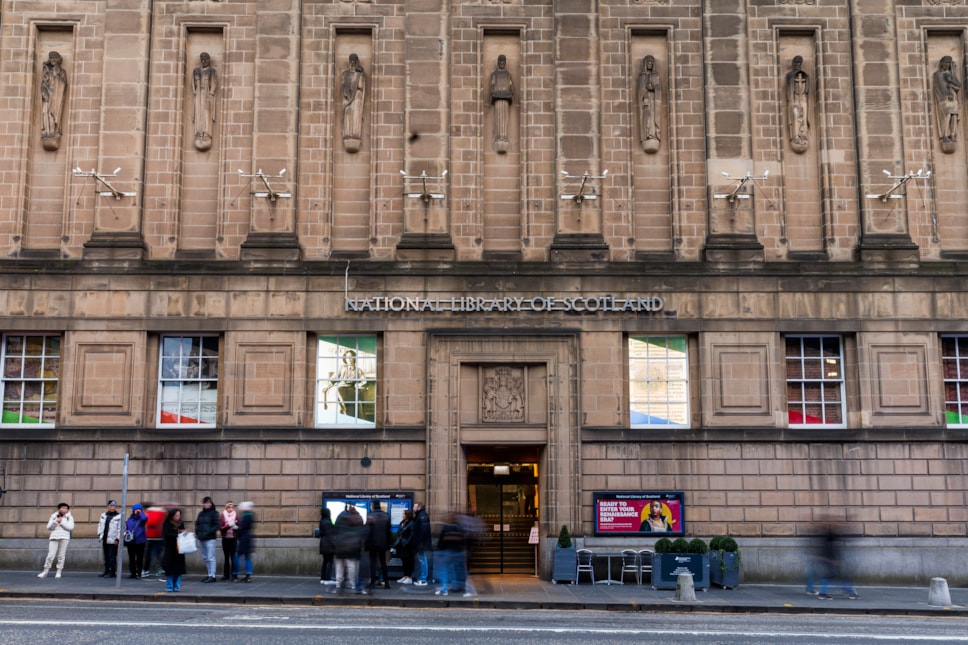 The facade of the George IV Bridge building, Edinburgh. People on the street look at information signs next to the main door.