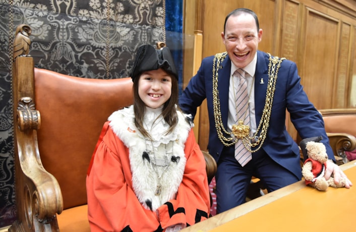 Children's Mayor of Leeds 1: Sienna is pictured in full mayoral red robe and black hat, sitting next to the Lord Mayor of Leeds, in blue suit and his gold chains.