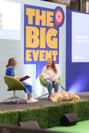 Lucy Edwards at Big Event: Image of Helen Dolphin and Lucy Edwards sat on stage at The Big Event. Lucy Edwards sits on right hand side with guide dog at her feet.