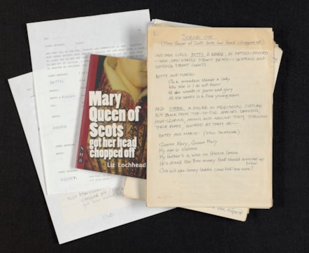 A collection of items photographed from above, including a script, a full play in the form of a book, and a manuscript of scene one of the play.