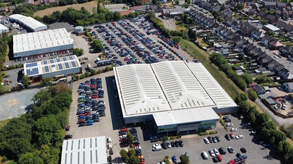 Motability Operations Coalville site aerial view: An aerial view showing a large white building at the centre which is surrounded by a large number of parked cars in various colours