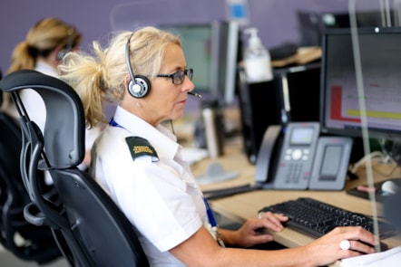 Side shot of person in white shirt with 'Senior clinical advisor' epaulette, wearing a headset in front of a screen and telephone.