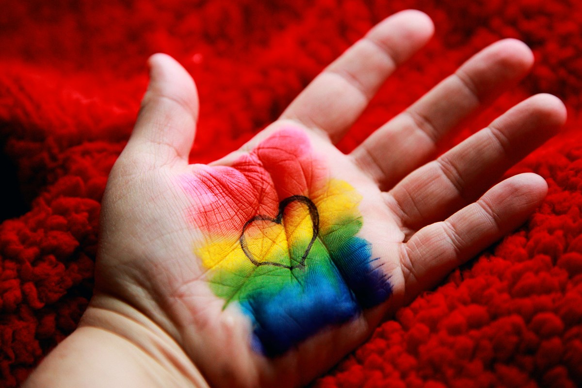 Rainbow paint and heart on palm of hand.